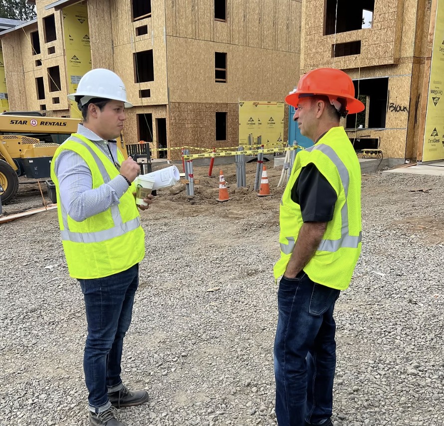 Two Leeway supervisors in high-visibility vests and hard hats reviewing plans at a multifamily construction site