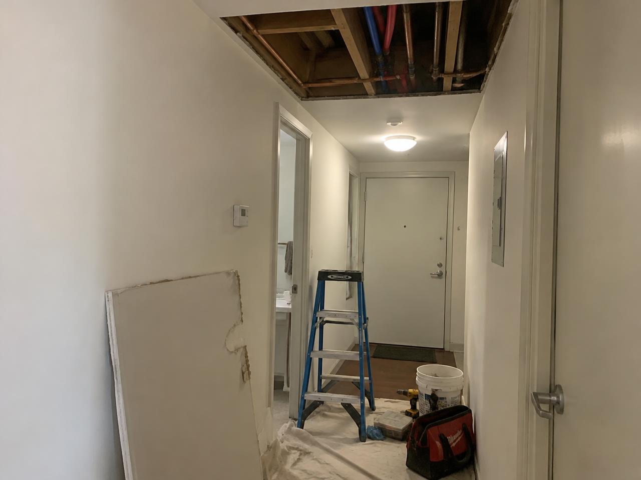 Open hallway ceiling exposing water lines during a plumbing and drywall repair in an apartment unit